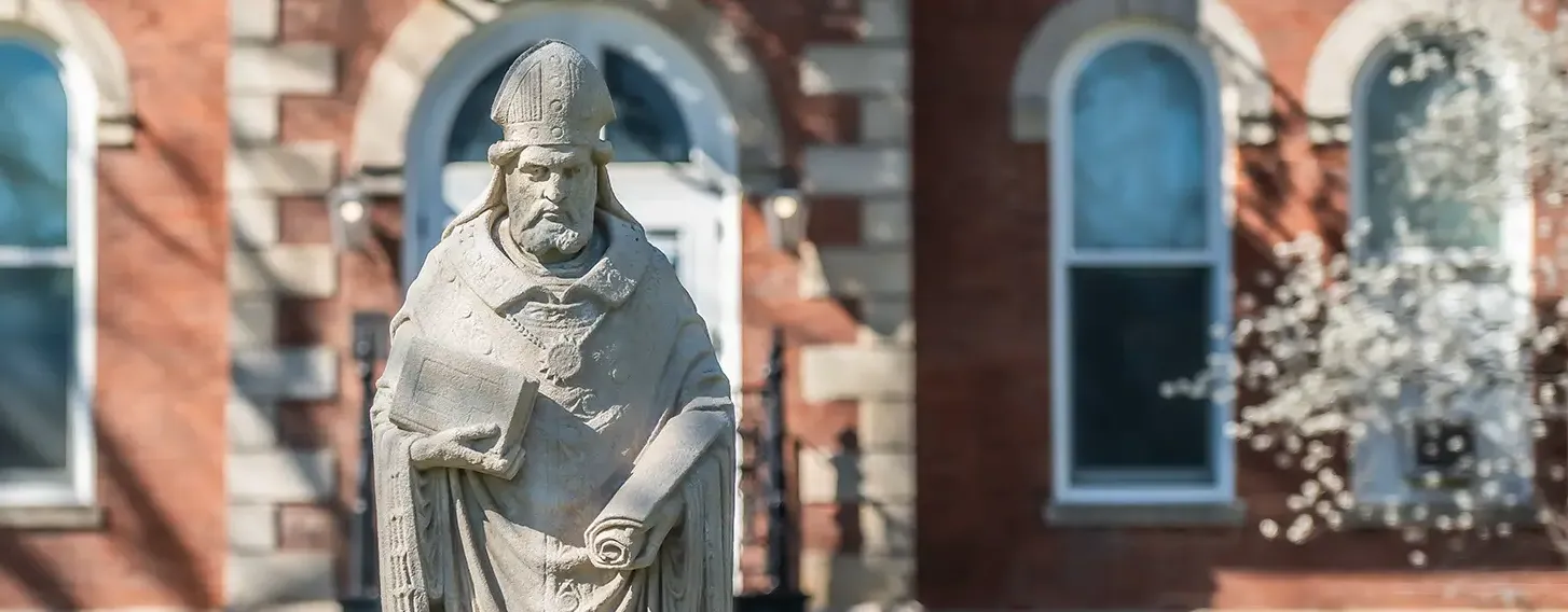 The statue of St. Ambrose in front of a brick building.