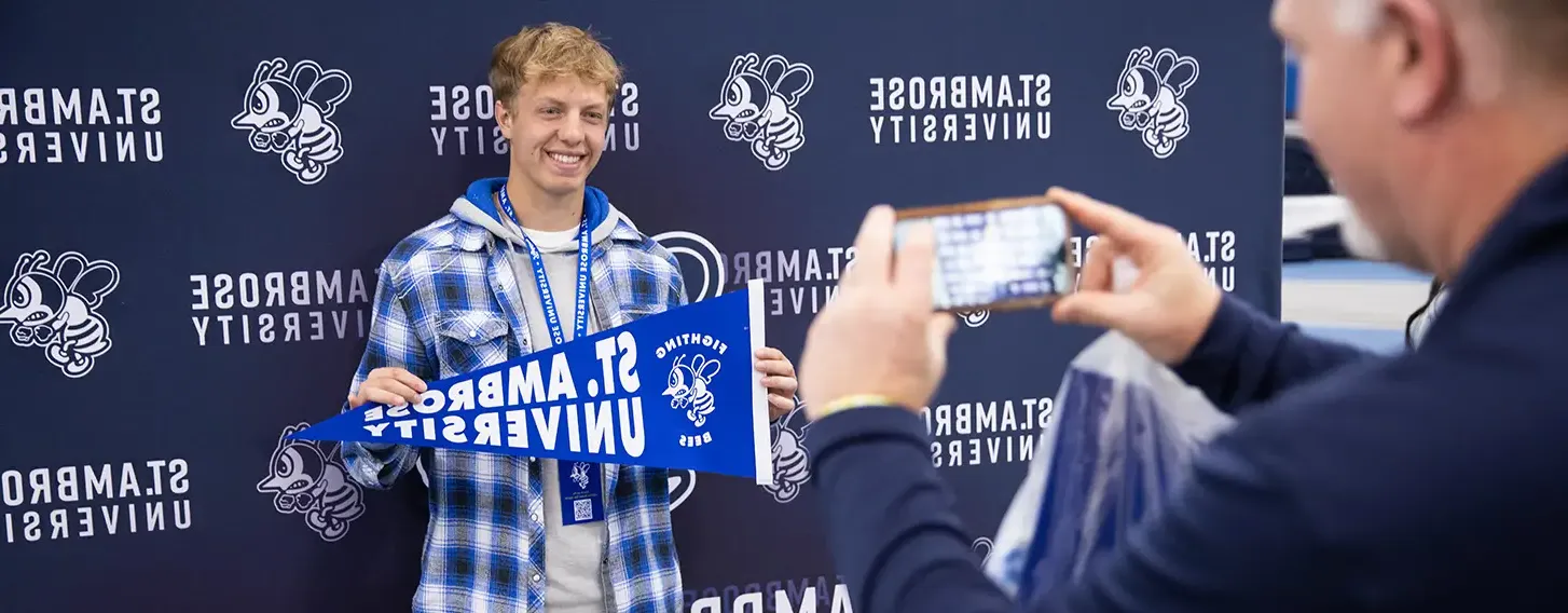 A student posing for a parent holding a St. Ambrose flag